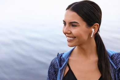 Photo of Young sportswoman with wireless earphones near river