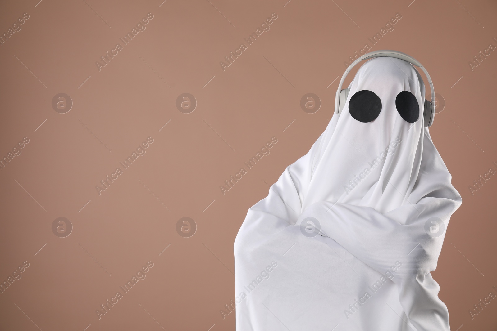 Photo of Person in ghost costume with headphones on dark beige background, space for text