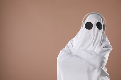 Person in ghost costume with headphones on dark beige background, space for text