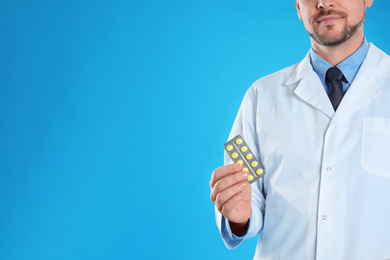 Photo of Professional pharmacist with pills on light blue background, closeup. Space for text