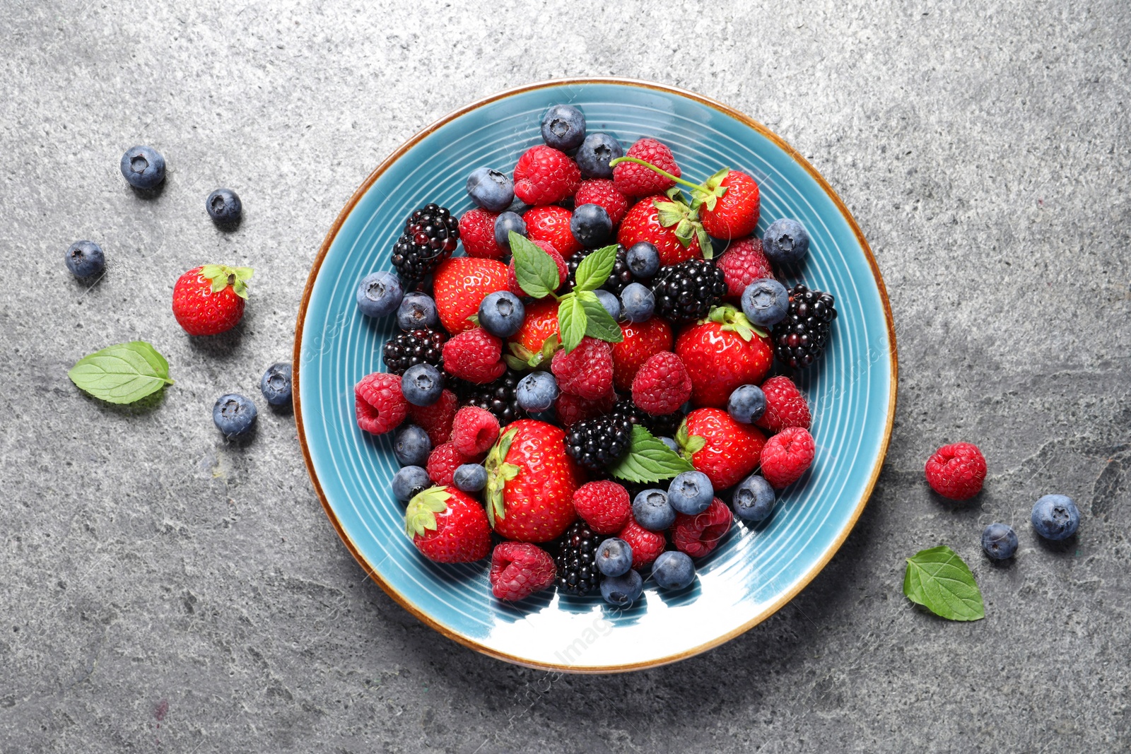 Photo of Many different fresh ripe berries in plate on grey table, flat lay