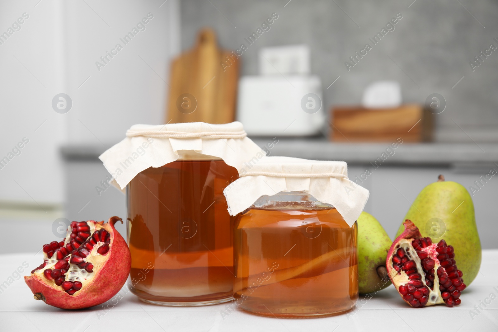 Photo of Homemade fermented kombucha and fresh fruits on white table in kitchen