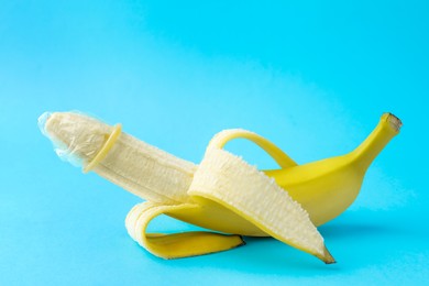 Photo of Banana with condom on light blue background. Safe sex concept