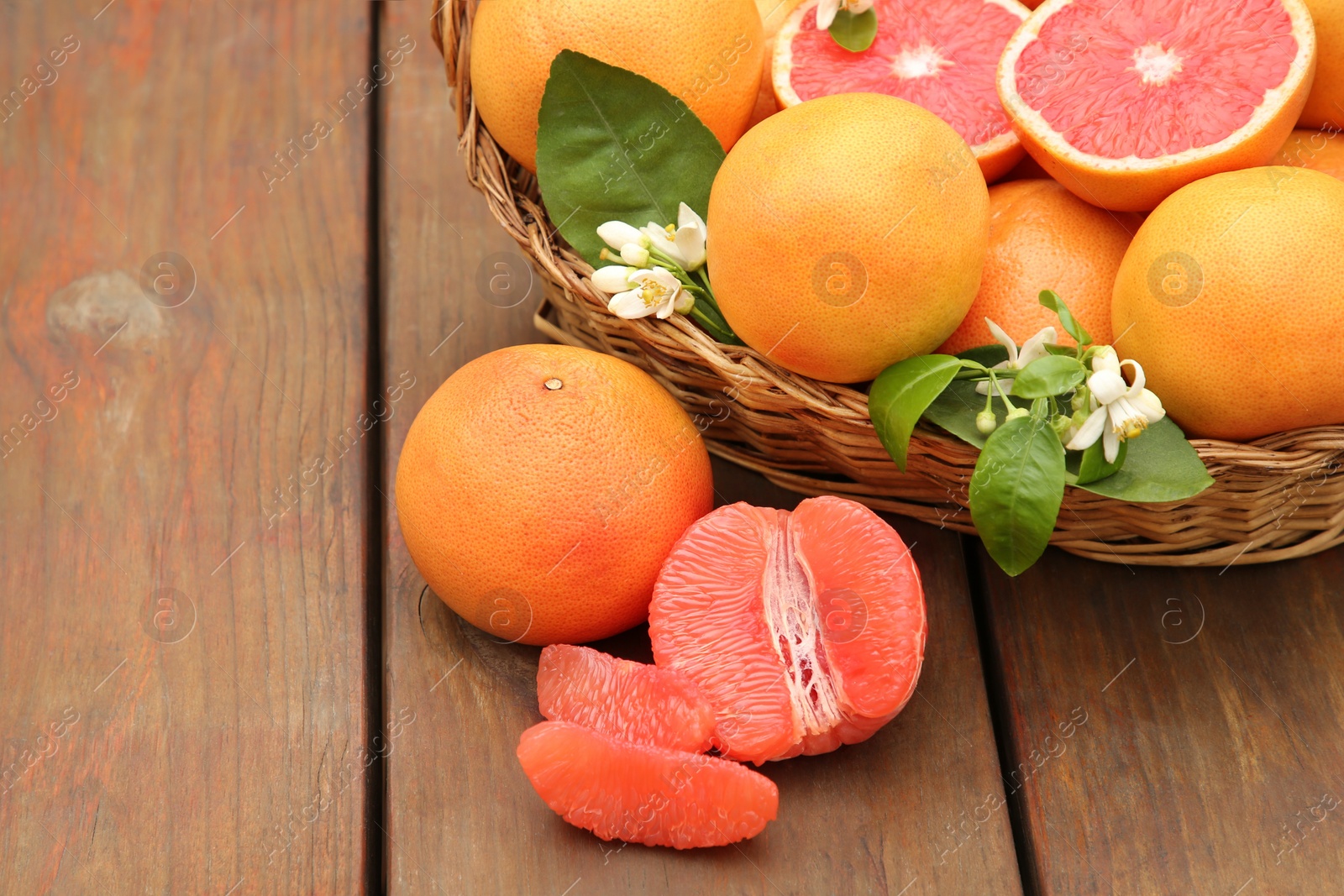 Photo of Wicker basket with fresh grapefruits and green leaves on wooden table