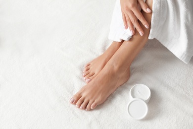 Woman with beautiful feet and moisturizing cream on white towel, closeup. Spa treatment