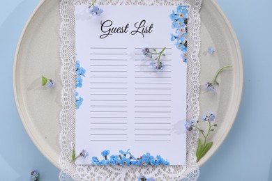 Plate with guest list, lace and flowers on light blue background, top view. Space for text