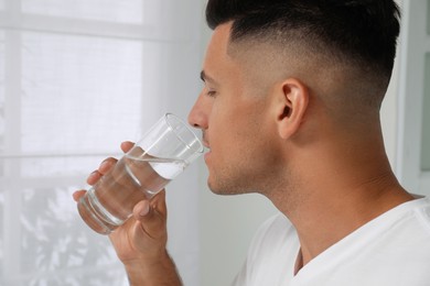 Man drinking tap water from glass at home, closeup