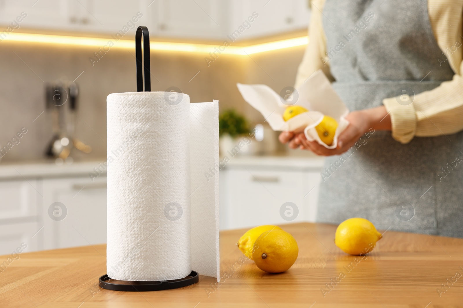 Photo of Woman wiping lemons with paper towels in kitchen, closeup, focus on table