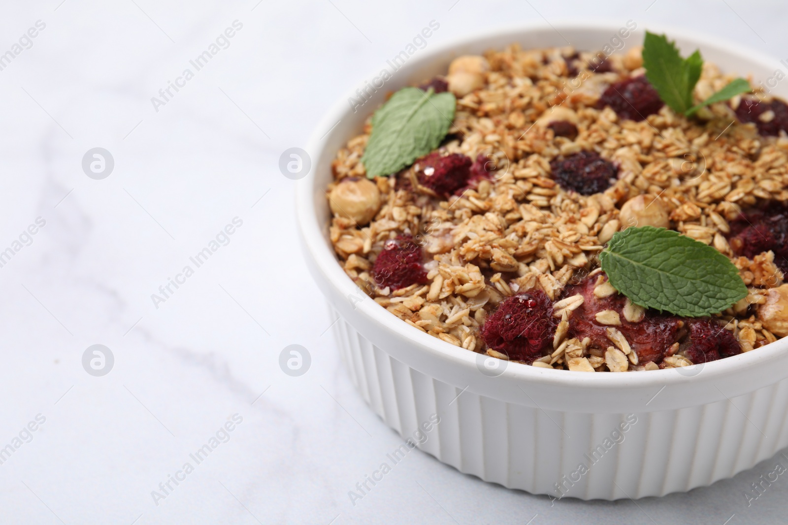 Photo of Tasty baked oatmeal with berries and nuts on white marble table, closeup. Space for text