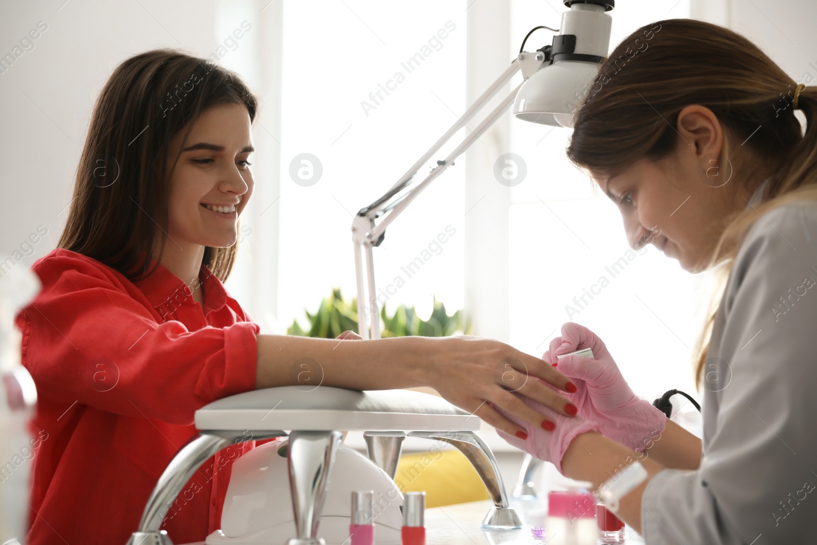 Photo of Professional manicurist applying polish on client's nails in beauty salon