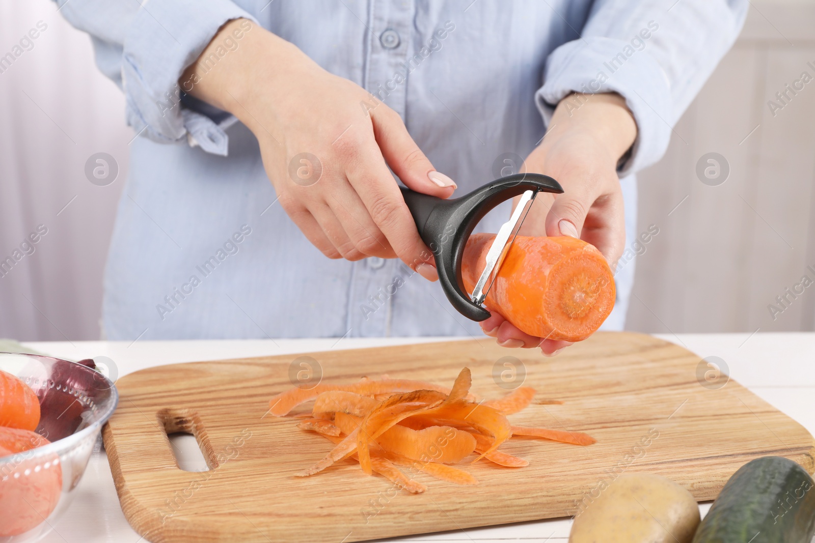 Photo of Woman peeling fresh carrot at table indoors, closeup