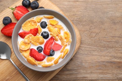 Bowl of tasty crispy corn flakes with milk and berries on wooden table, flat lay. Space for text