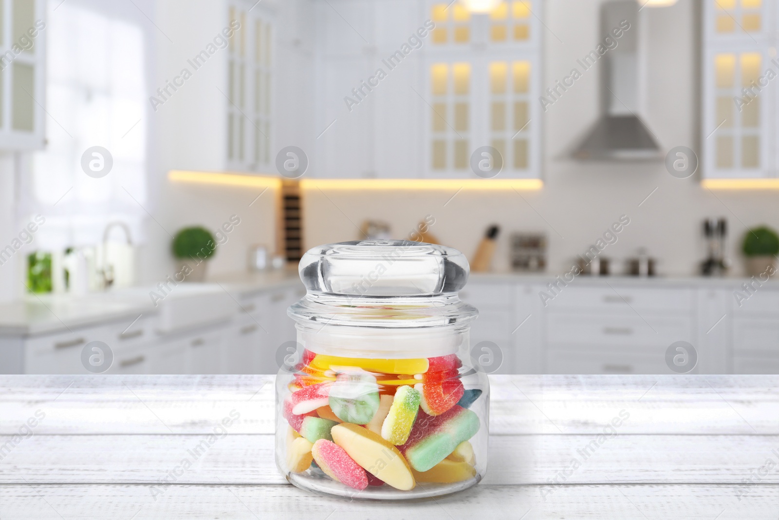 Image of Glass jar with tasty gummy candies on white wooden table in kitchen