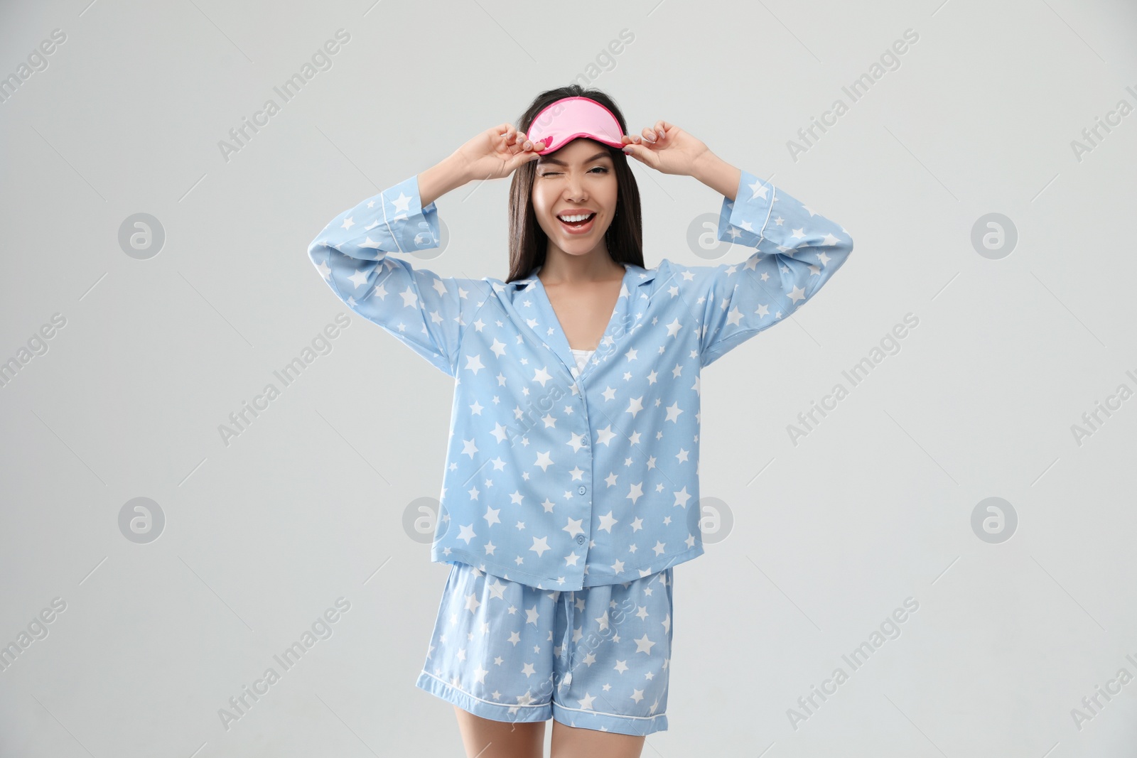 Photo of Beautiful Asian woman wearing pajamas and sleeping mask on light grey background. Bedtime