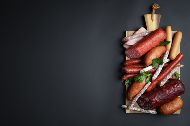 Photo of Different types of sausages served on black background, top view. Space for text]