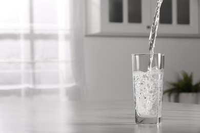 Photo of Pouring water into glass at table indoors, space for text