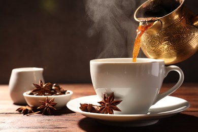 Photo of Pouring aromatic hot coffee into cup and anise stars on wooden table. Space for text