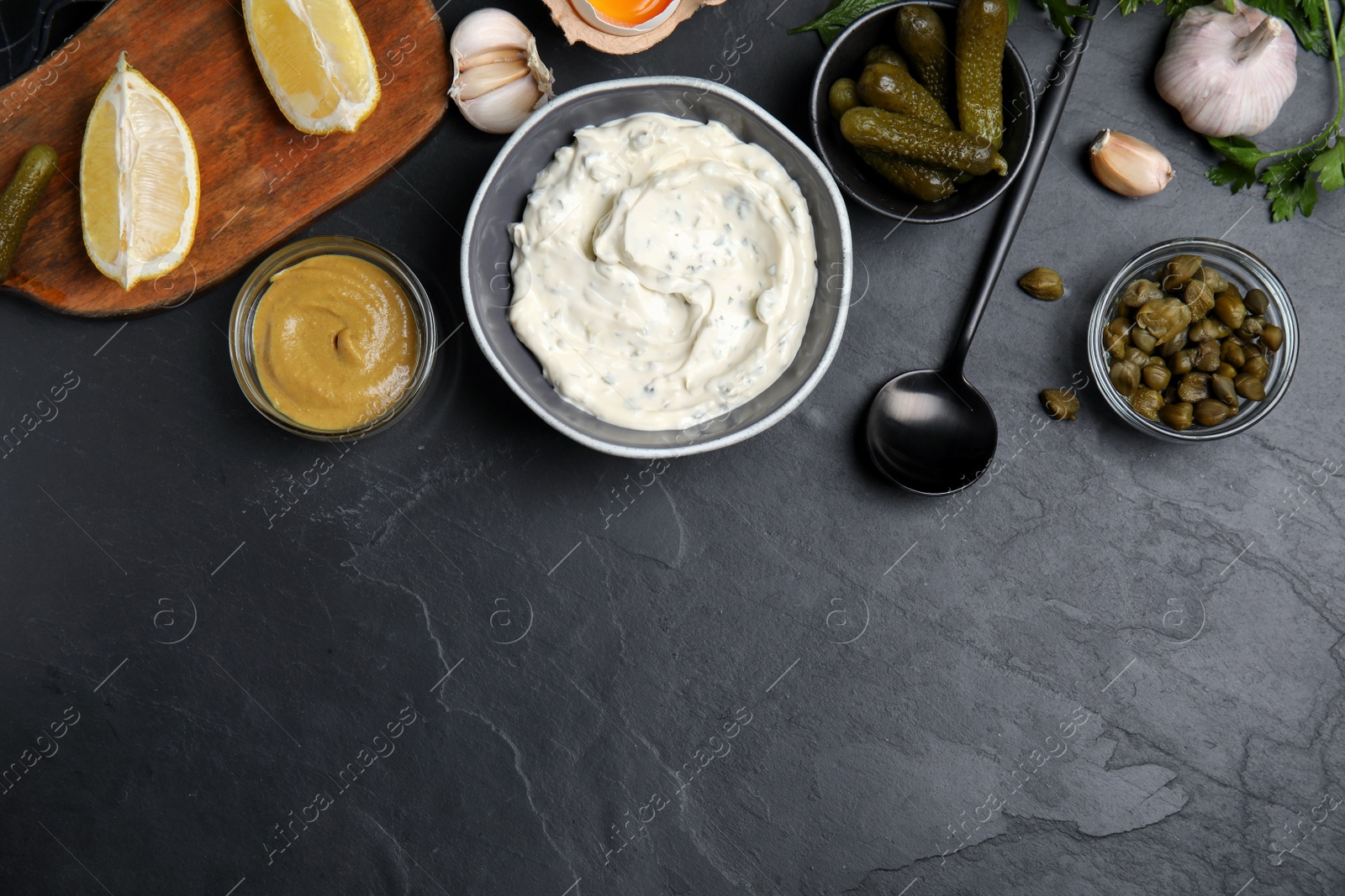 Photo of Tasty tartar sauce and ingredients on black table, flat lay. Space for text