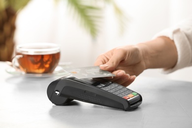 Woman using terminal for contactless payment with credit card in cafe