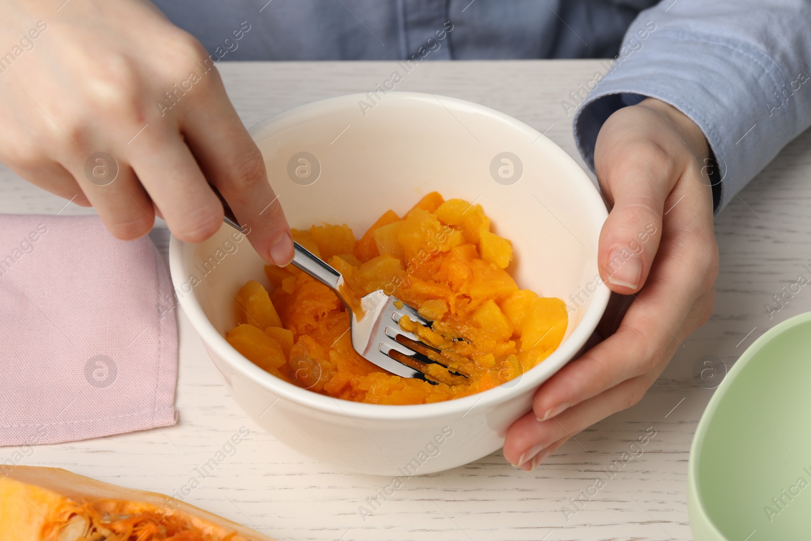 Photo of Woman making baby food with pumpkin at white wooden table, closeup