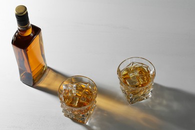 Photo of Whiskey with ice cubes in glasses and bottle on white table, above view