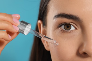 Young woman applying serum onto her face on light blue background, closeup