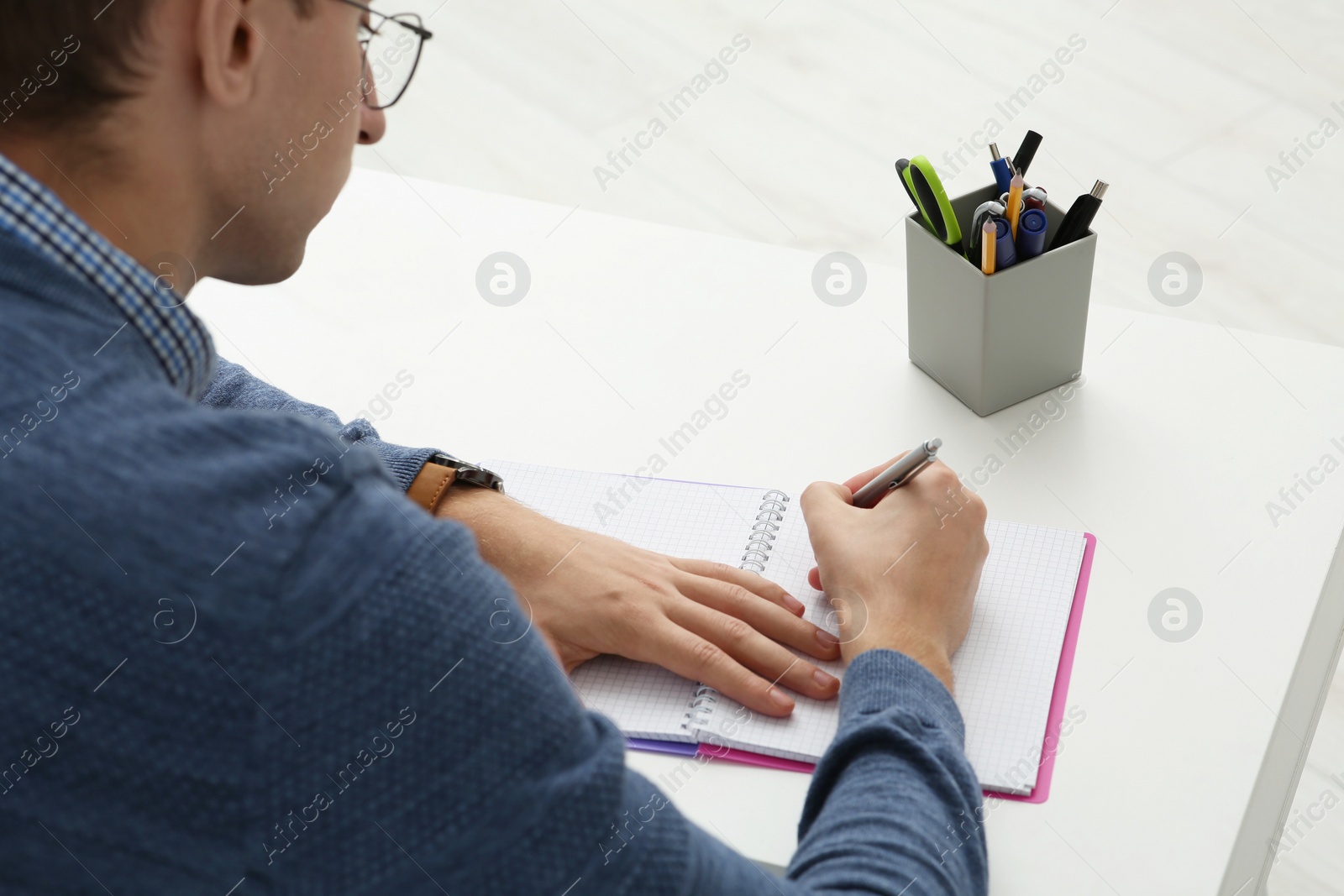 Photo of Man writing in notebook at white table indoors, closeup