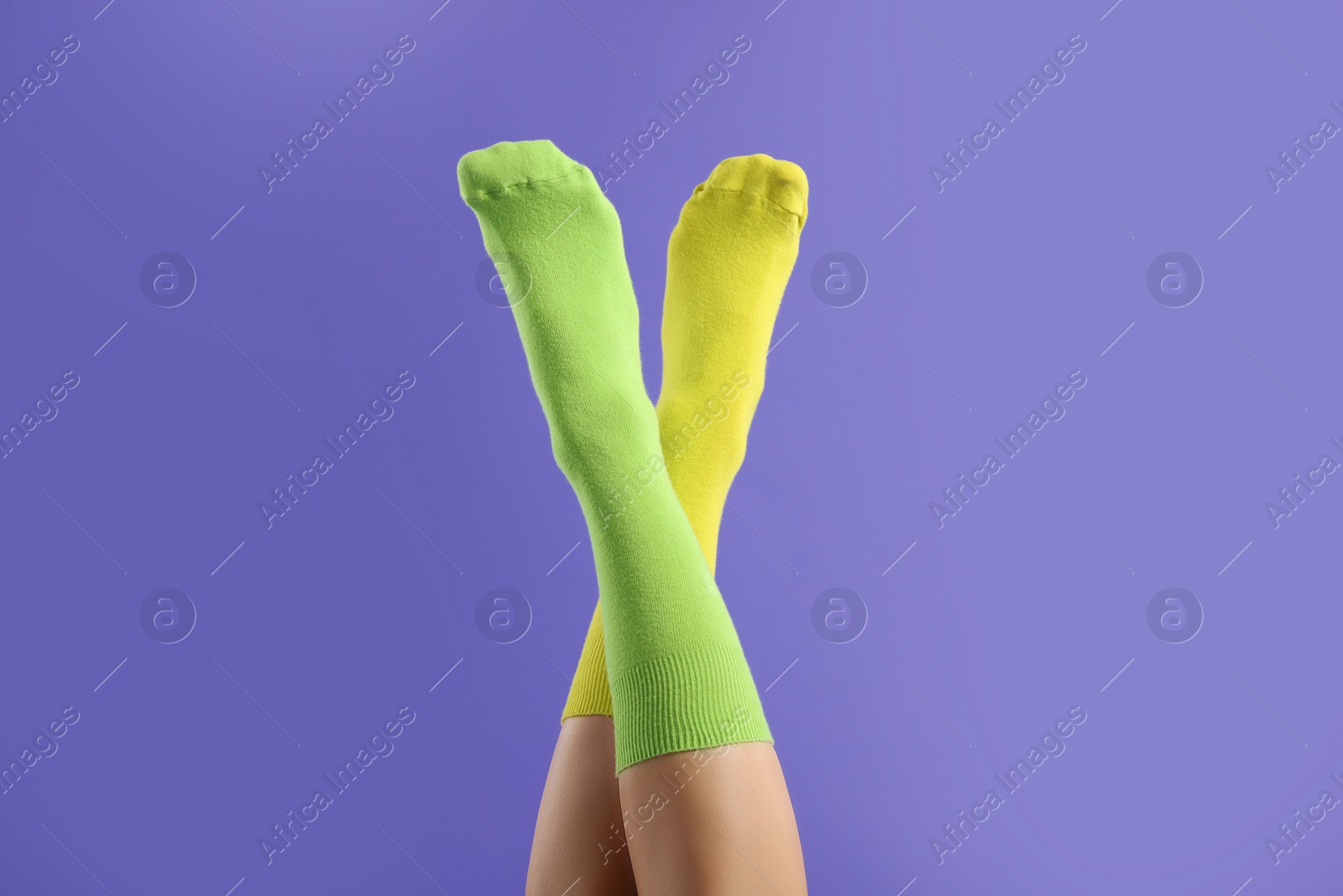 Photo of Woman in different stylish socks on violet background, closeup