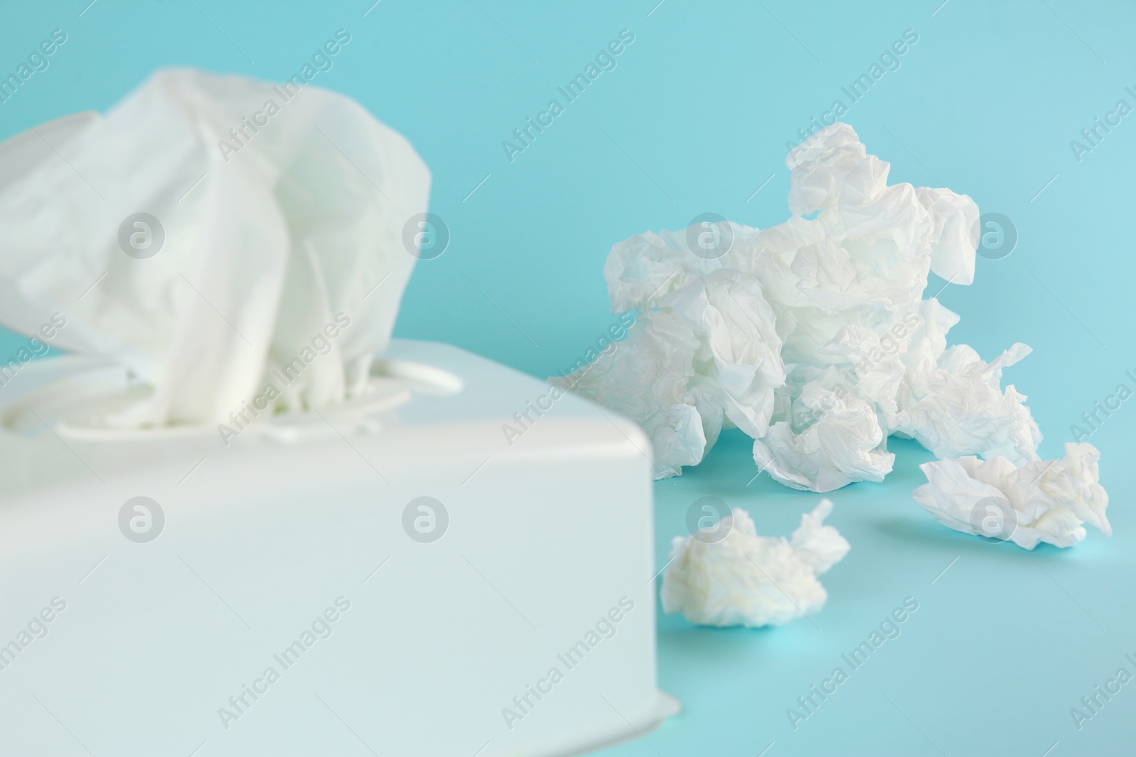 Photo of Used paper tissues and white holder on light blue background, closeup