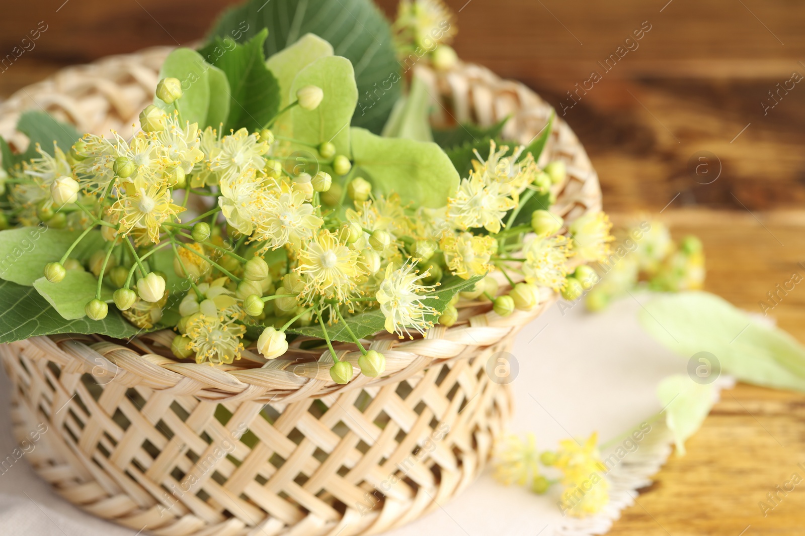 Photo of Fresh linden leaves and flowers in wicker basket on wooden table,