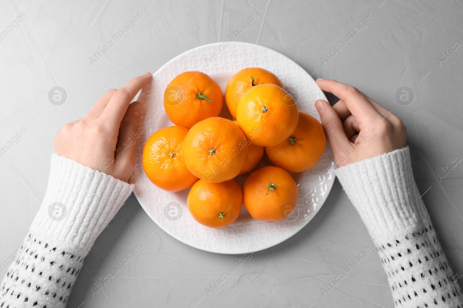 Photo of Woman with plate of fresh ripe tangerines at grey table, top view