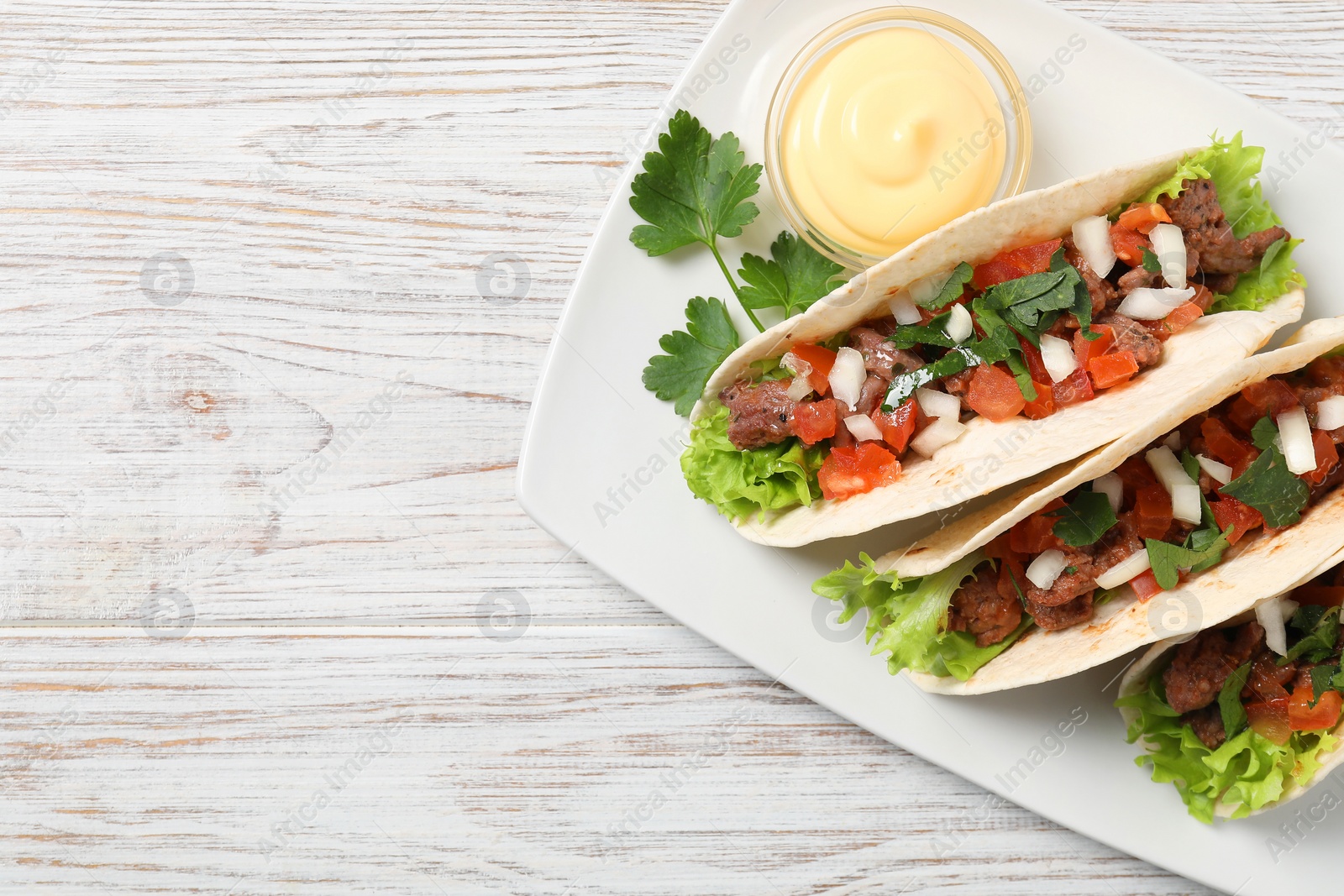 Photo of Delicious tacos with meat and vegetables served on wooden table, top view. Space for text