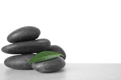 Photo of Stack of spa stones and green leaf on table against white background. Space for text