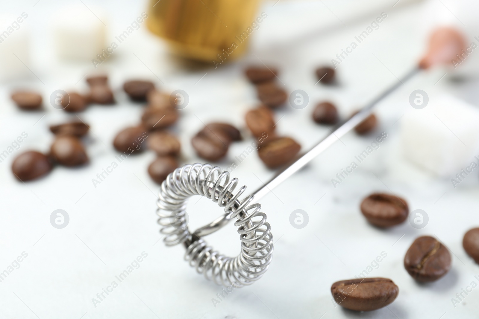 Photo of Milk frother wand and coffee beans on white marble table, closeup