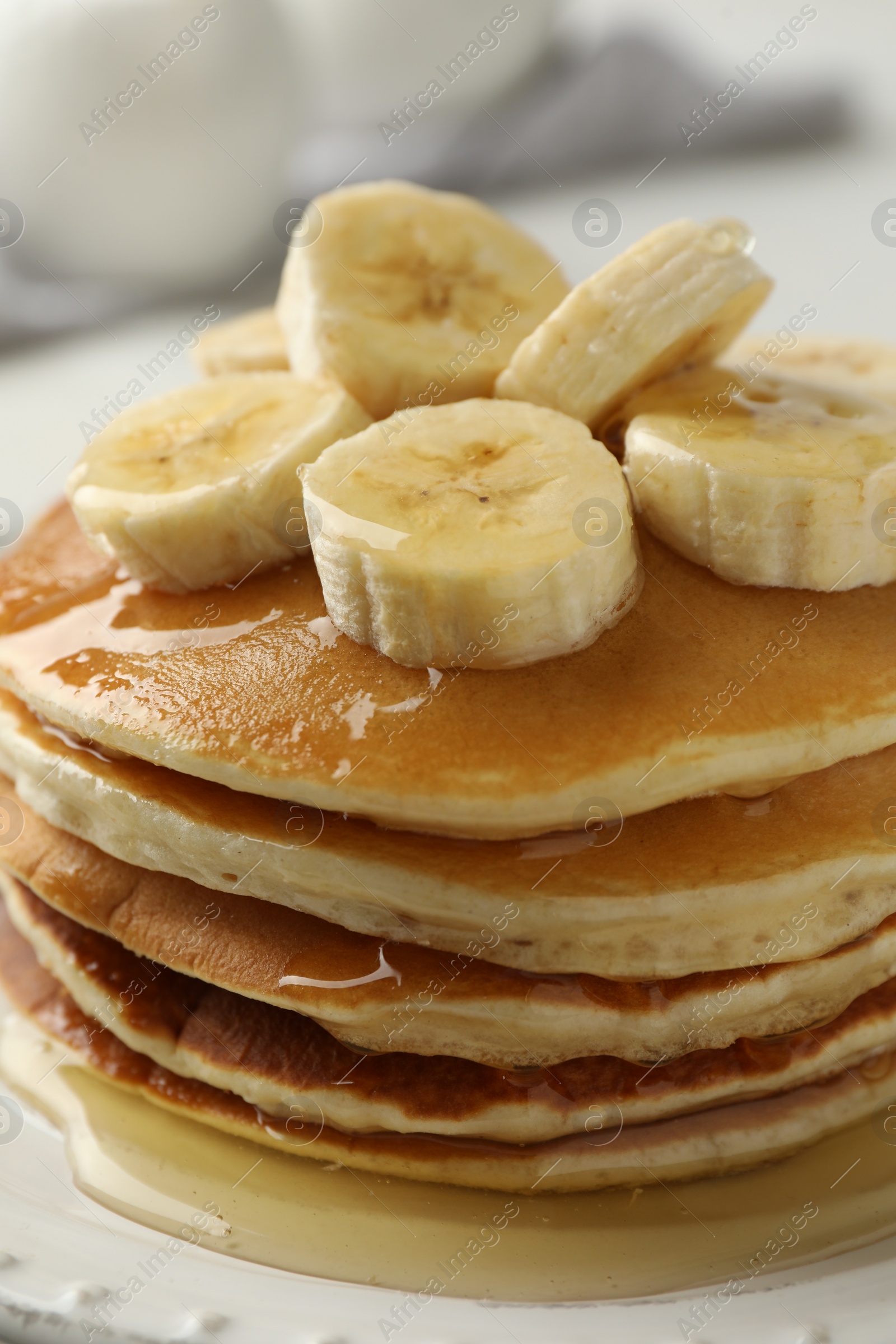 Photo of Delicious pancakes with bananas and honey on white table, closeup