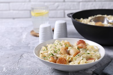 Delicious scallop pasta with spices in bowl on gray textured table, space for text