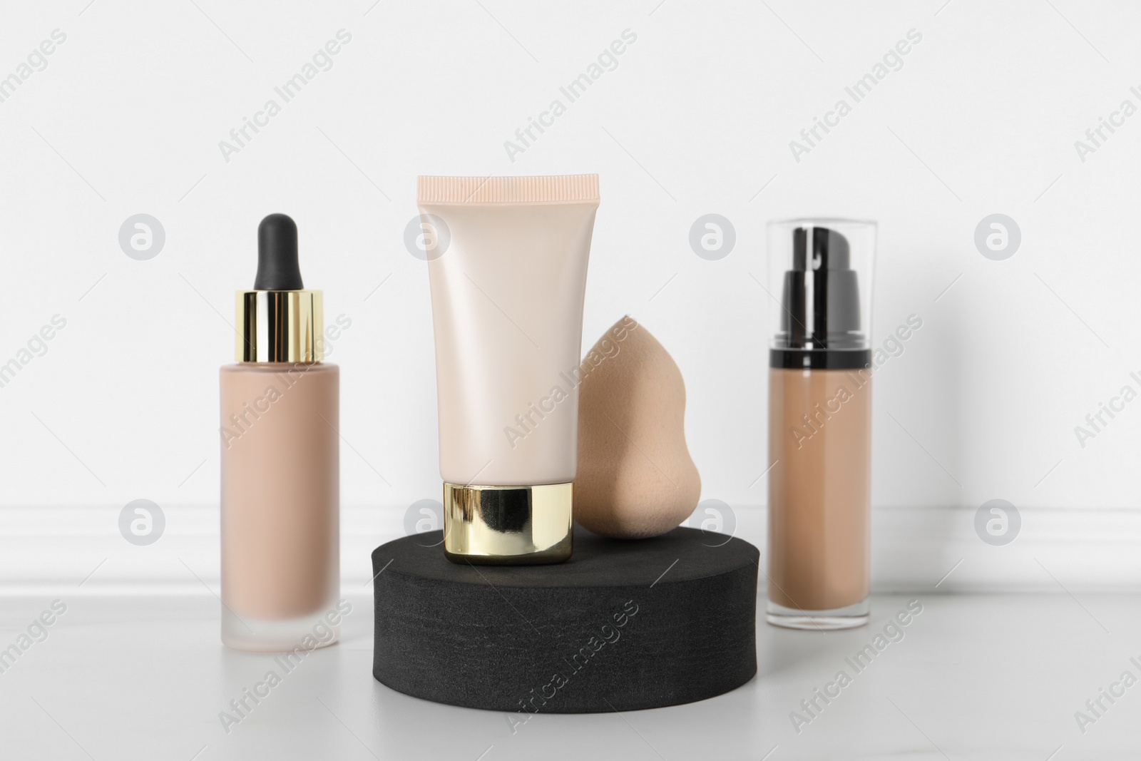 Photo of Makeup sponge, bottles and tube of skin foundation near white wall