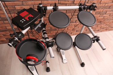 Photo of Modern electronic drum kit with headphones near red brick wall indoors, above view. Musical instrument