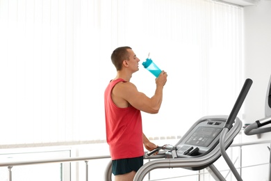 Photo of Athletic young man drinking protein shake on running machine in gym