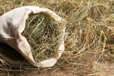 Photo of Dried hay in burlap sack on wooden table, closeup