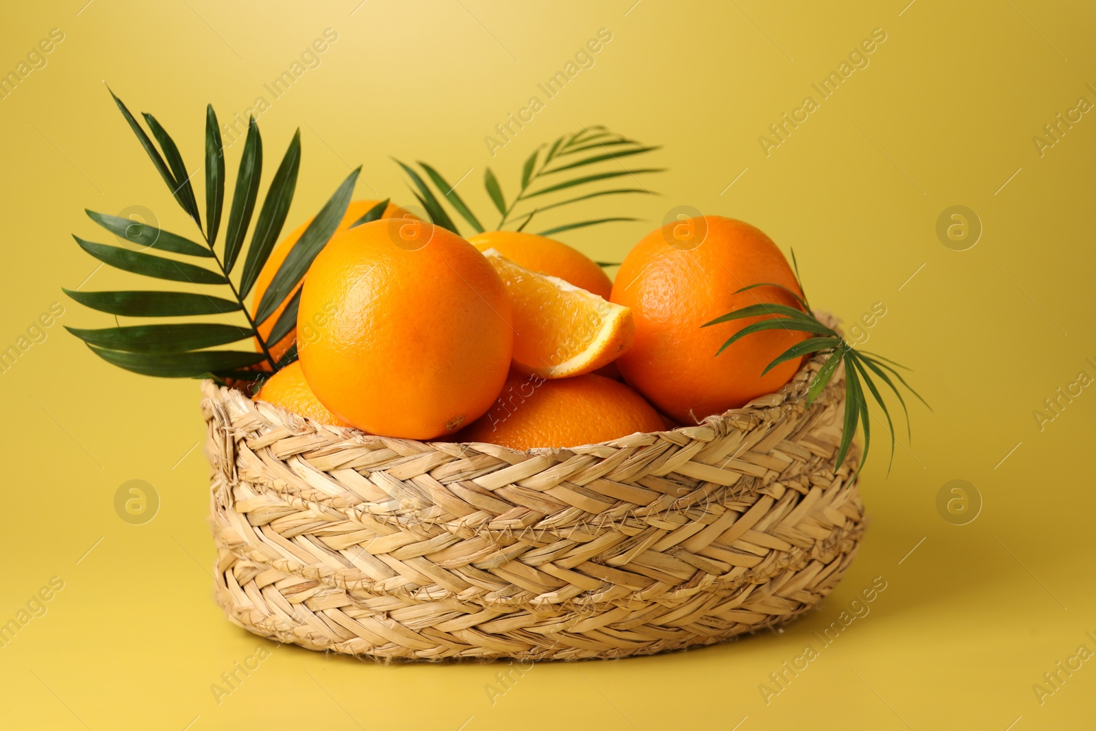 Photo of Fresh oranges in wicker basket on yellow background, closeup