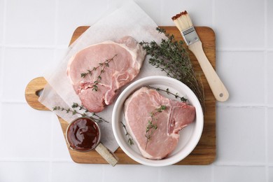 Photo of Raw meat, thyme, basting brush and marinade on white tiled table, top view