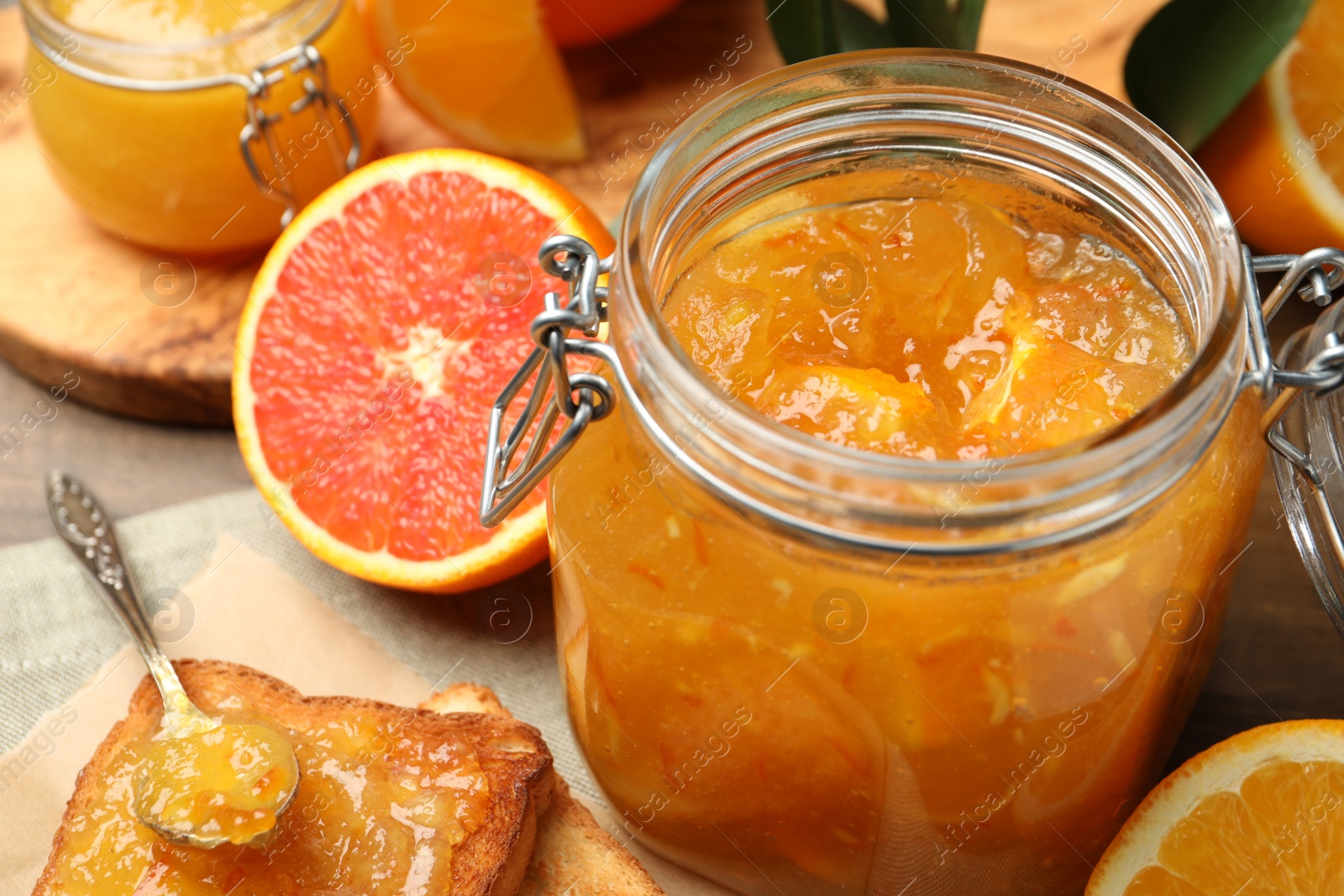 Photo of Delicious orange marmalade in jar, fresh fruits and toasts on table, closeup