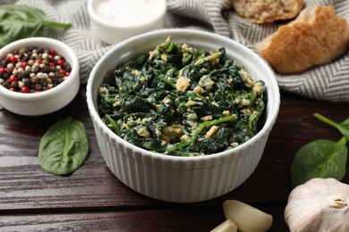 Photo of Tasty spinach dip with egg in bowl, spices and bread on wooden table, closeup