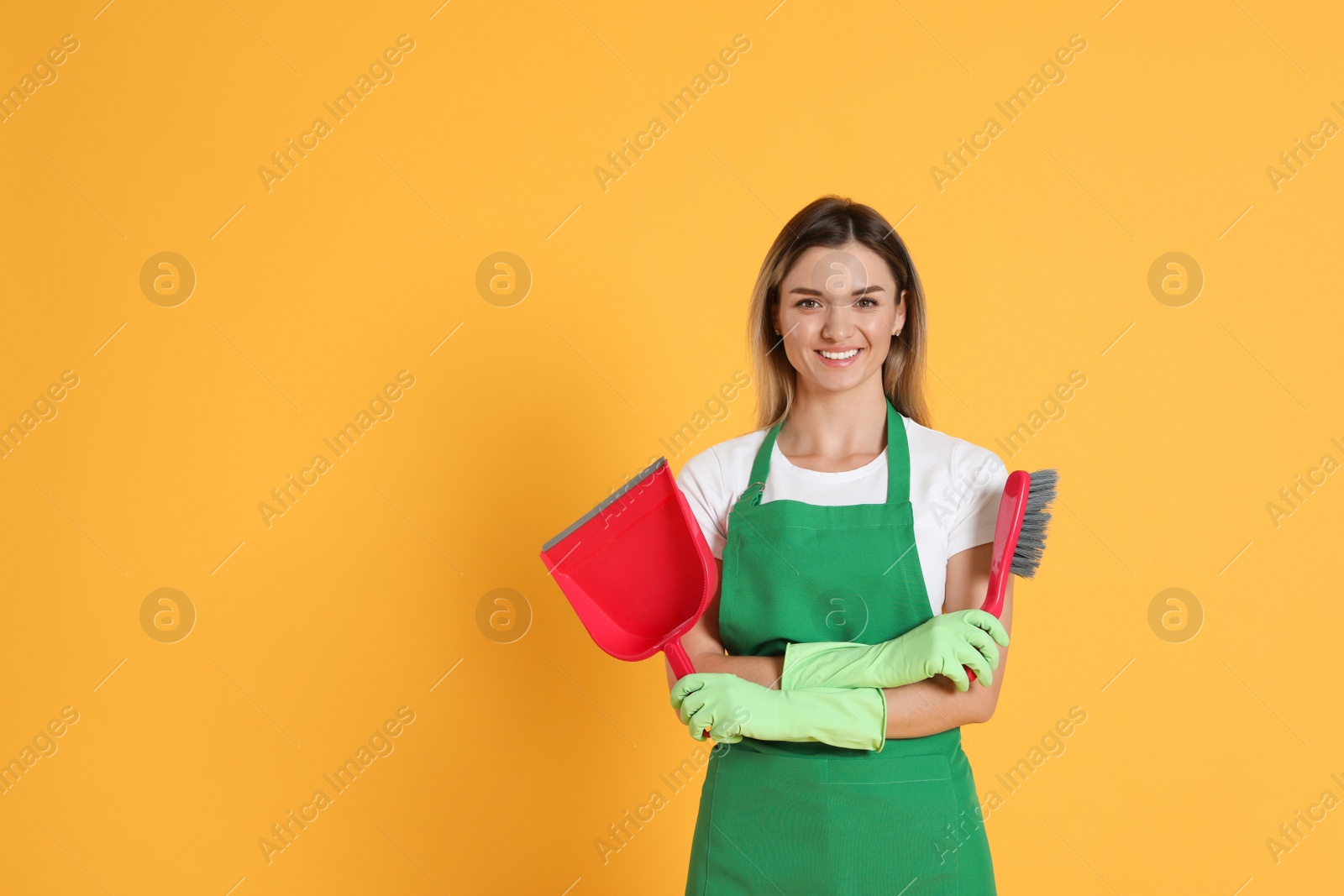 Photo of Young woman with broom and dustpan on orange background, space for text