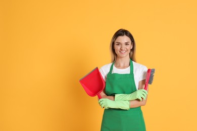 Young woman with broom and dustpan on orange background, space for text