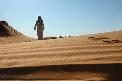 Man in arabic clothes walking through desert on sunny day, back view