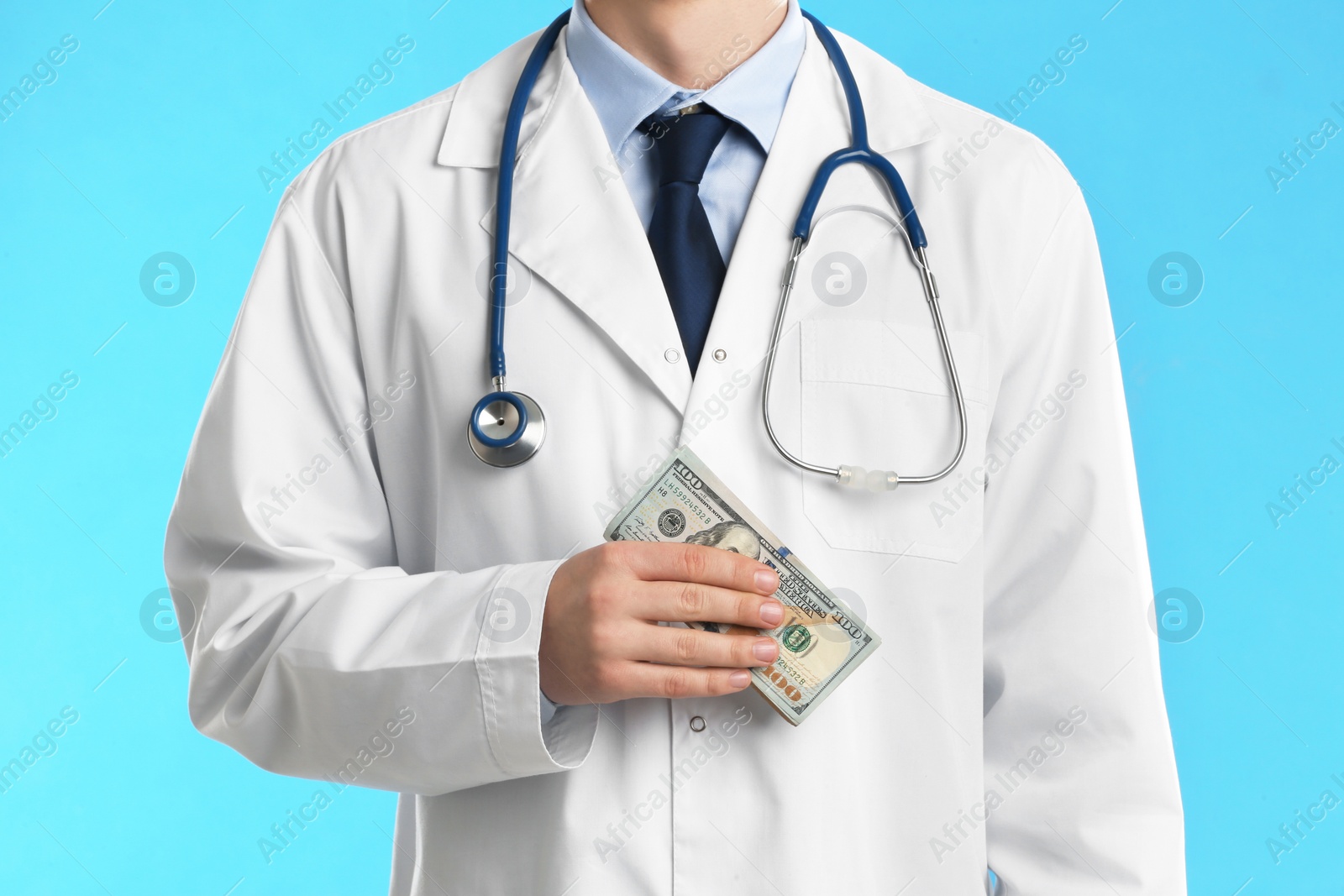 Photo of Doctor with bribe on light blue background, closeup. Corruption in medicine