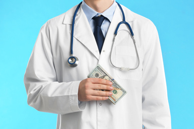 Doctor with bribe on light blue background, closeup. Corruption in medicine