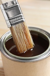 Photo of Dipping brush into can with varnish on table, closeup